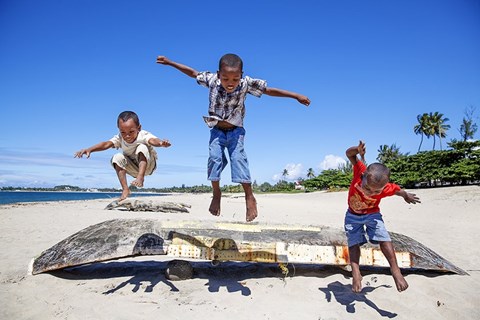 drei Jungen, die am Strand über ein Boot springen